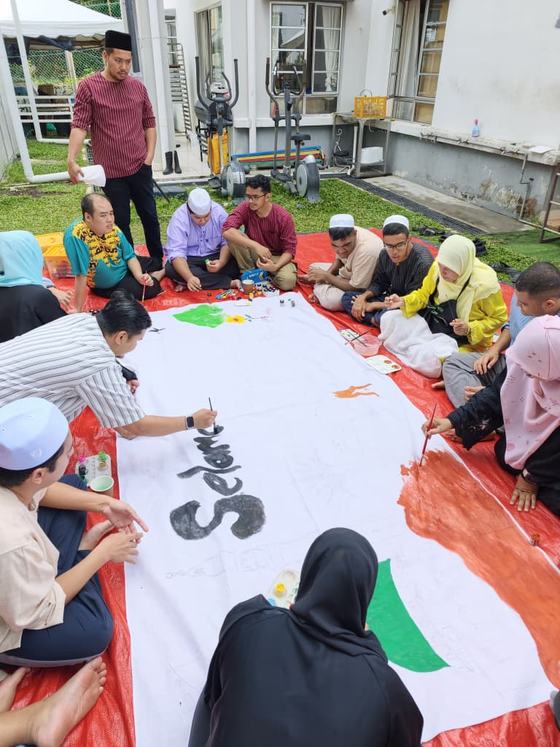 Tulisan sambutan sedang diwarnakan di tengah sepanduk oleh pelatih bersama pembimbing.