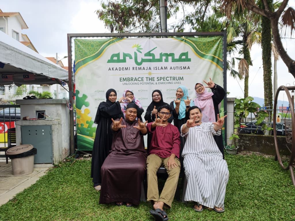 Warga ARISMA bergambar di hadapan sepanduk akademi bertulis Embrace the Spectrum.